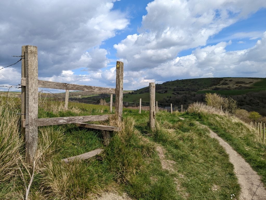 a wooden stile on a hill with grassy hills in the background