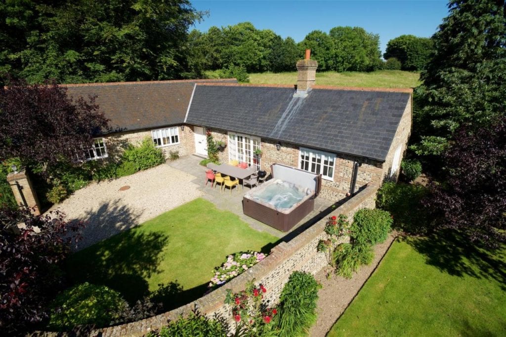 drone shot looking down at a row of stone holiday cottages with grey slate roofs. a wall encloses a garden with a lawn, hot tub, and table and chairs. 5 star hotels in dorset.