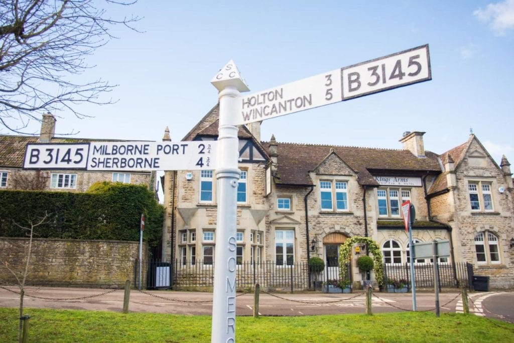 white metal signpost for milborne port and sherborne with a historic country pub behind built from beige coloured stone