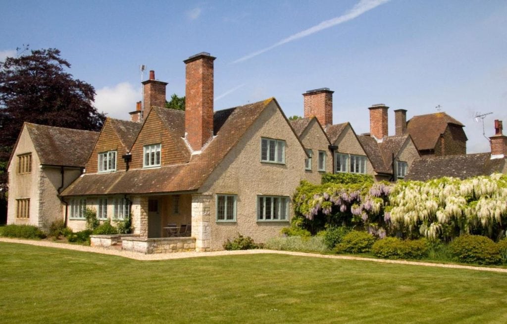 large country manor house on a green lawn, with beige coloured stone walls and red tiled roof