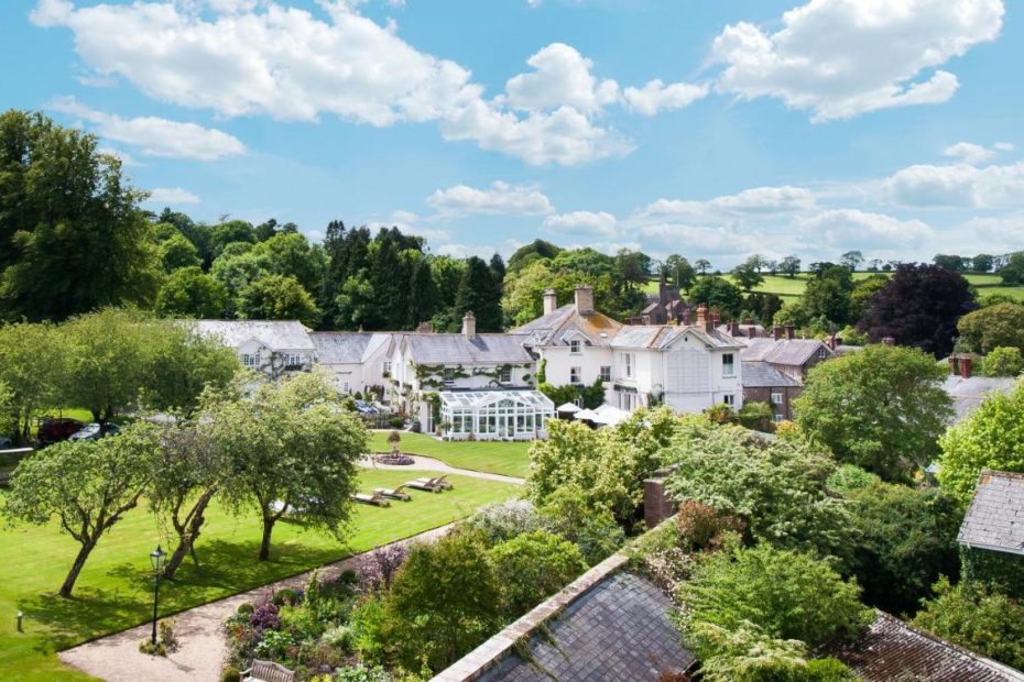 aerial shot of a large white country manor with a large greenhouse surrounded by lawns and trees - best 5 star hotels in dorset