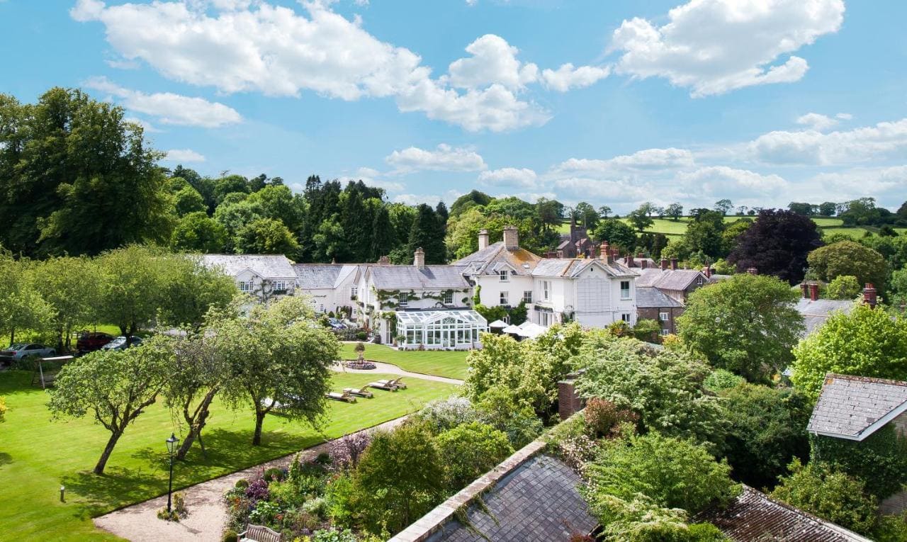 aerial shot of a large white country manor with a large greenhouse surrounded by lawns and trees - best 5 star hotels in dorset