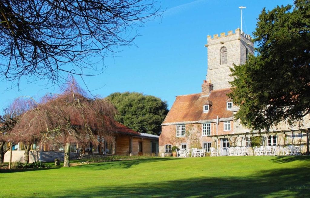 red brick country manor house with a clock tower behind and a neat lawn in front. 