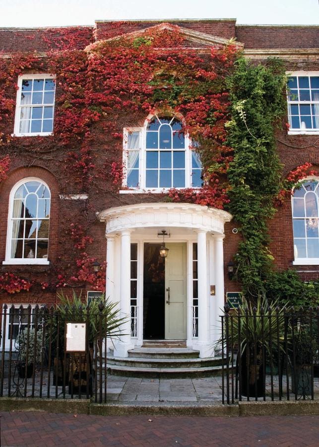 exterior of a red brick hotel covered in red ivy with white columns around the doorway
