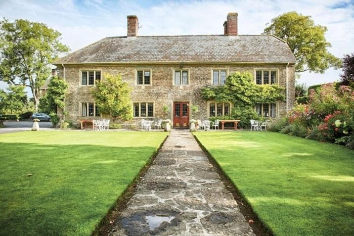 path leading through a green lawn towards a beige stone country house with a grey slate roof - dog friendly hotels dorset