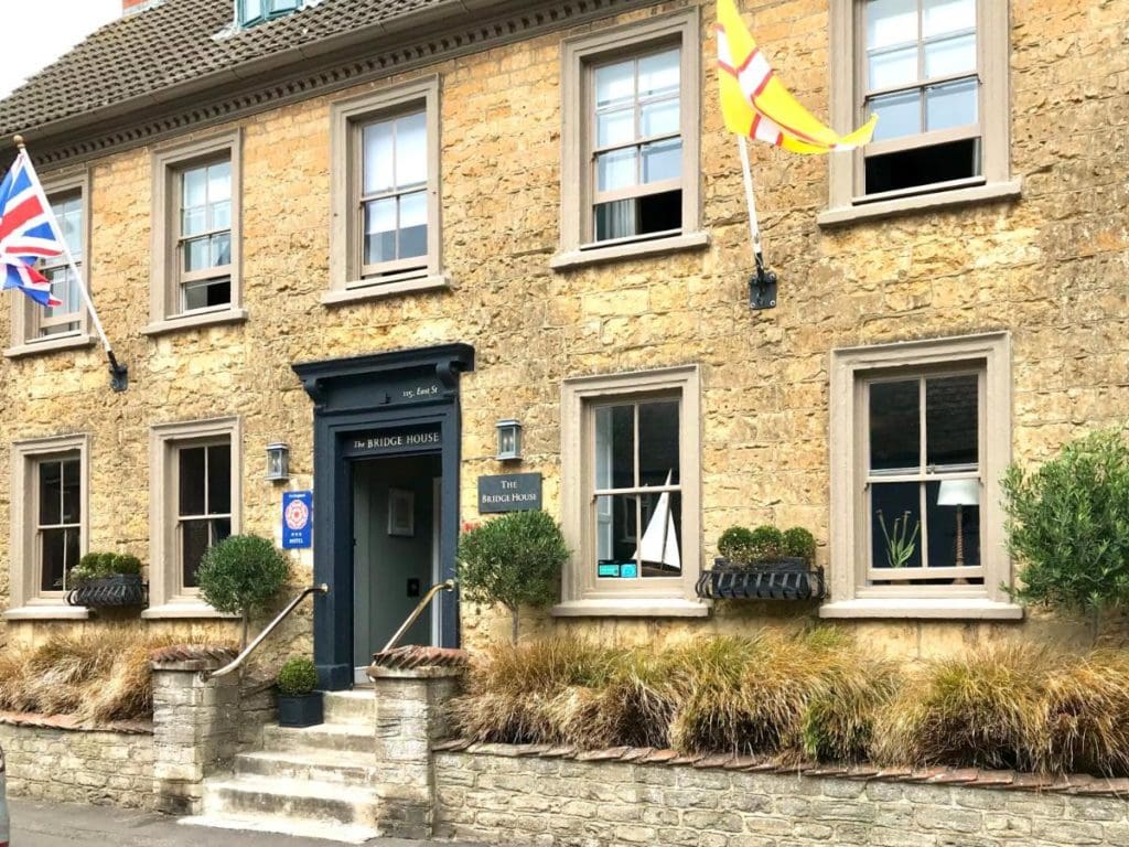 front of a beige stone hotel in bridport with the uk and dorset flags flying on either side of the door - dog friendly hotels dorset