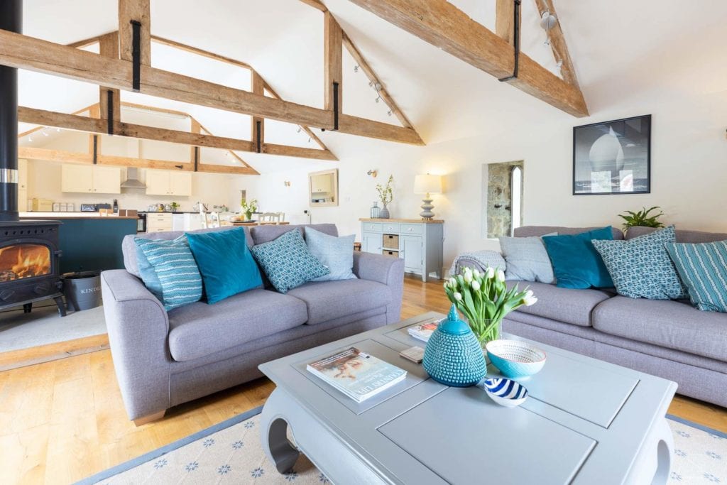 interior of a large barn conversion with white walls and light pine wooden beams with two large pale blue sofas and a light blue coffee table in the foreground and white walls behind. Best Holiday Cottages in Dorset