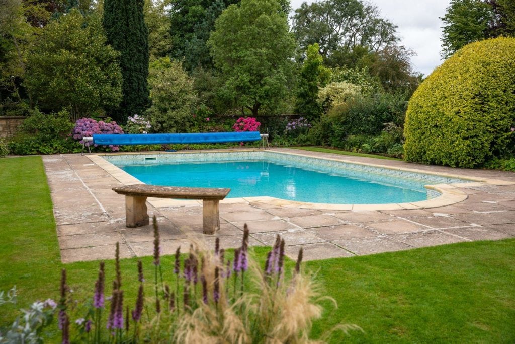small outdoor swimming pool in a garden with a grass lawn around it and lots of green behind. best holiday cottages in dorset. 