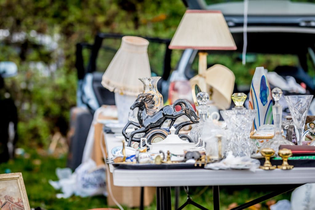 white trestle table outdoors in a park laden with bric a brac like old lamps and ornaments at a flea market. Car Boot Sales in Dorset. 