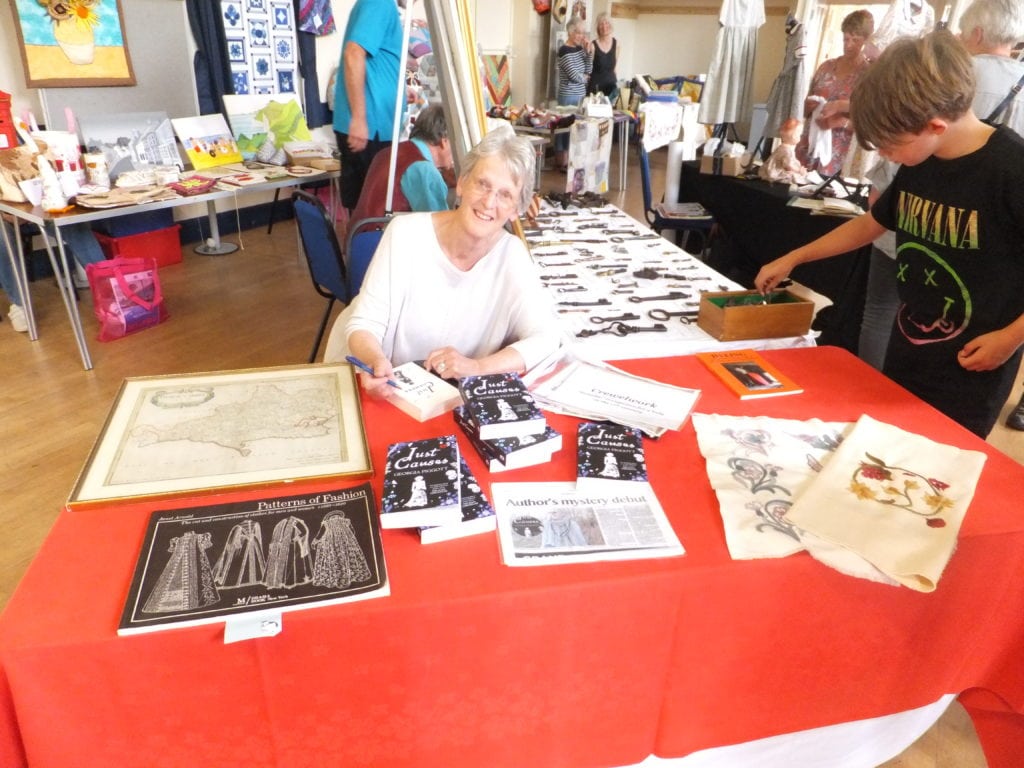 Georgia Piggott sitting at a red table with books signing a page and smiling at the camera