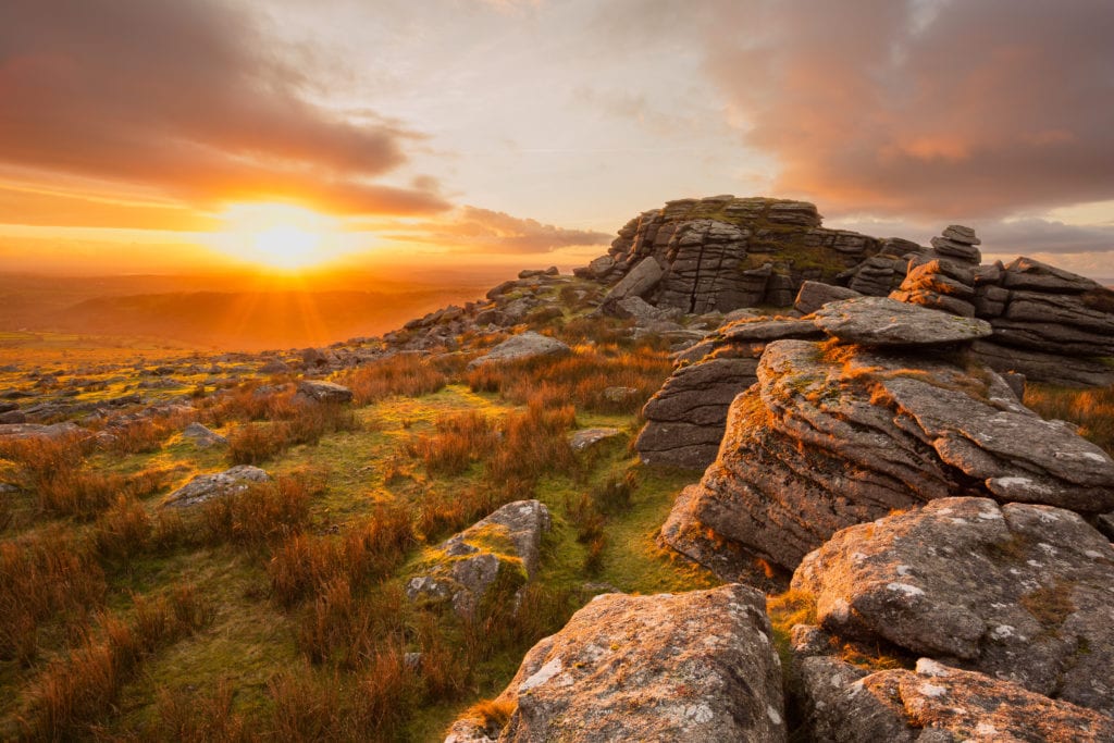Sunset from King's tor Dartmoor with several large grey stone boulders on top of a grassy hill 