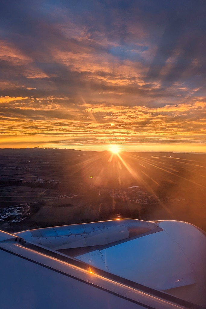 view from a plane window of the engine as the plane heads towards land with the sun setting over the horizon. Doret airports guide. 