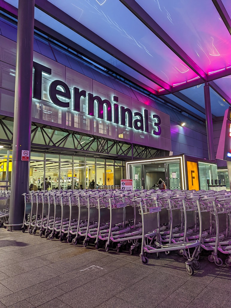 line of luggage trolleys in front of a doorway beneath a large sign Terminal 3 sign at Heathrow airport