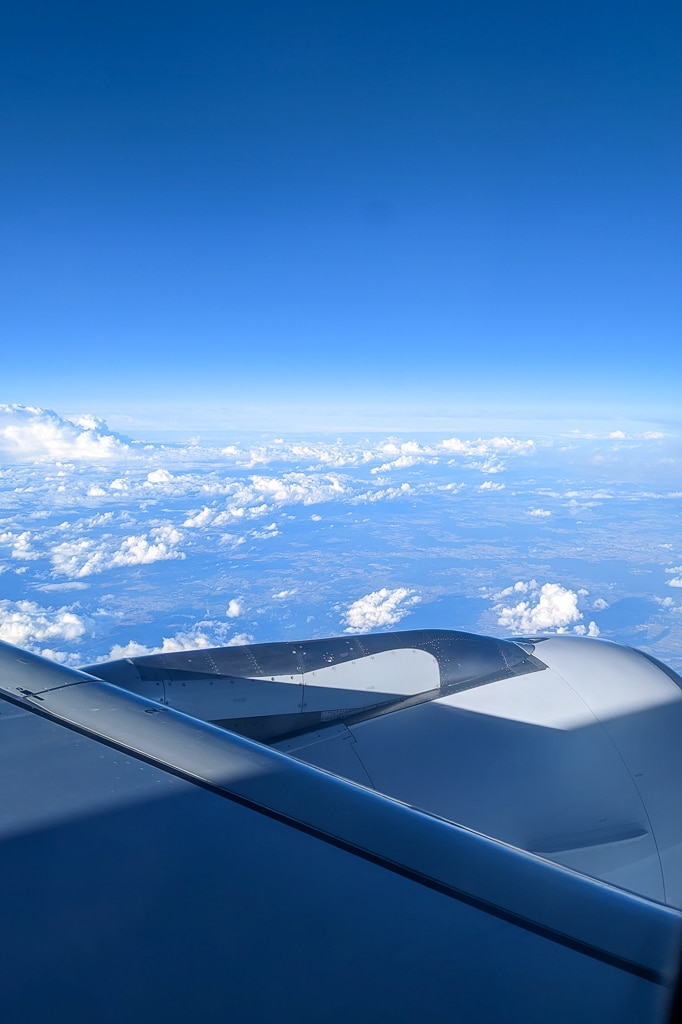 plane wing in the sky with blue sky above and clouds below