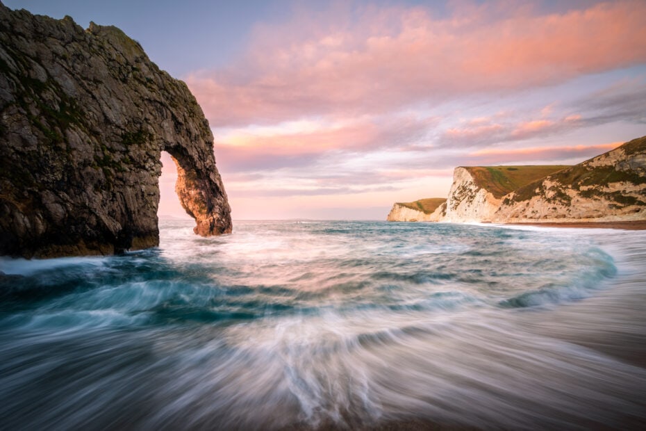natural stone archway over the sea in a small bay at sunset with pink clouds above