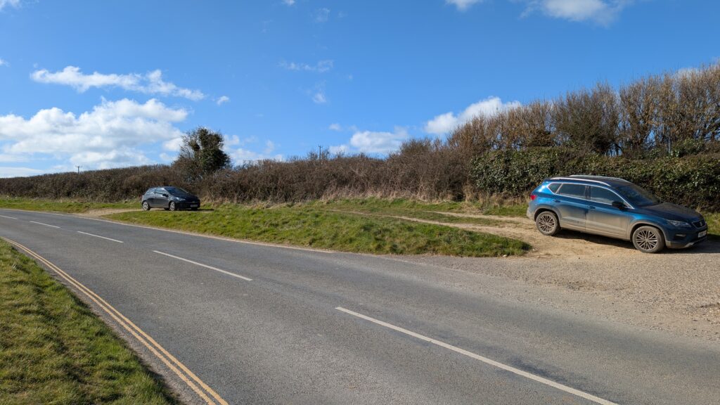 Empty road in the countryside in Dorset with 2 cars parked in a layby on a sunny day with blue sky. 