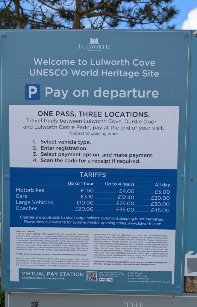 Large blue sign for Lulworth Cove Car Park with information about parking tarriffs and rules etc. 