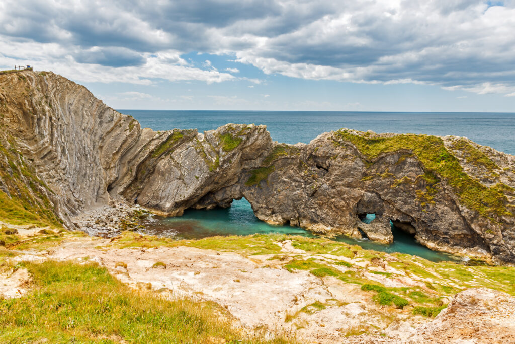 Low grey cliffs with folded rock layers and small caves passing through with the sea on the other side