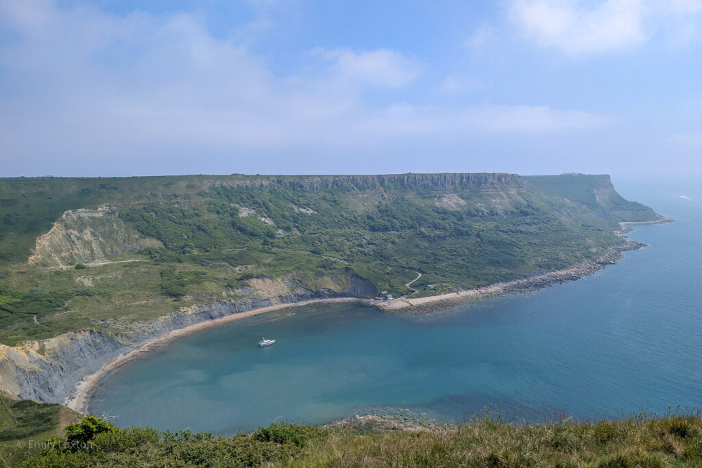 View from a cliff top of a semi circular cove surrounded by tall grassy cliffs. Chapman's Pool walk.