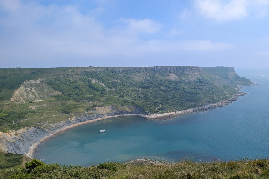 View from a cliff top of a semi circular cove surrounded by tall grassy cliffs. Chapman's Pool walk.