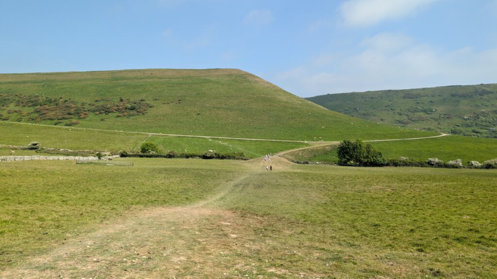 grass path leading across a grassy field towards a hill