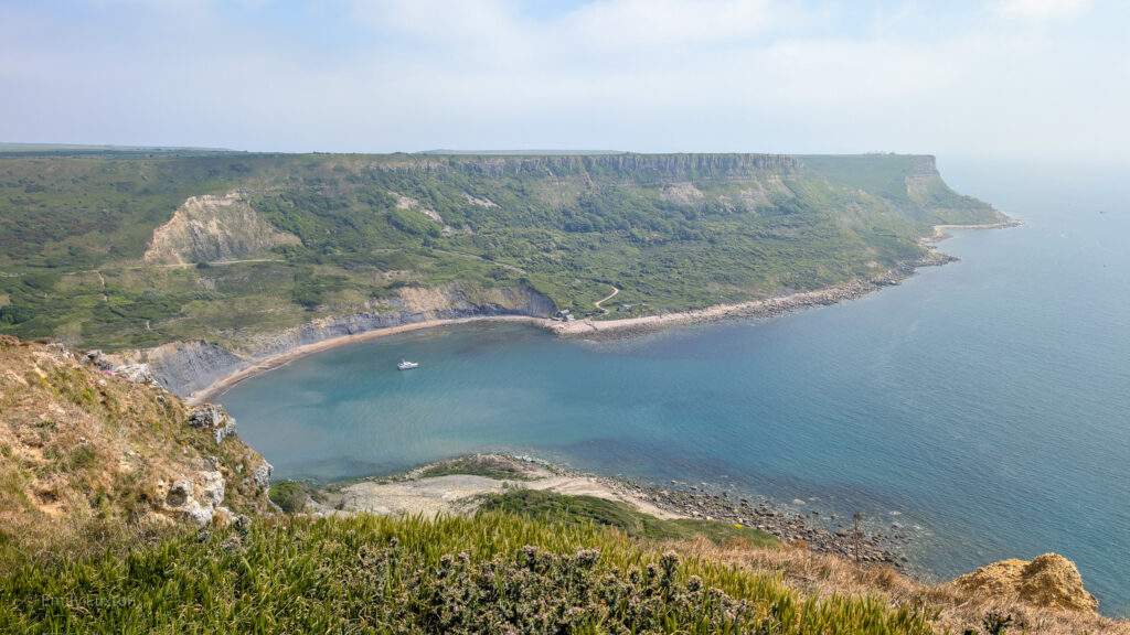 View from a cliff top of a semi circular cove surrounded by tall grassy cliffs. Chapman's Pool walk. 