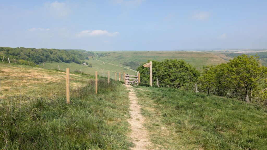 Dirt path in a grassy field leading towards a wooden stile