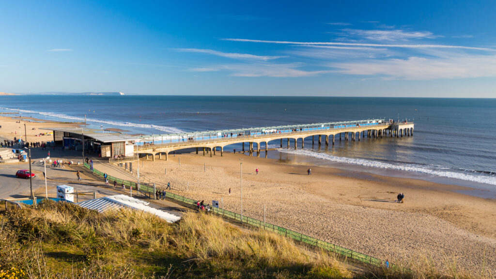 Overlooking a long pier running into the sea at Boscombe with a white sandy beach on either side. 
