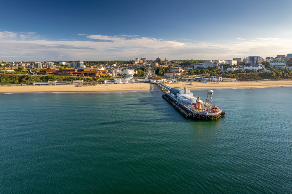 Aerial view of Bournemouth pier taken from above the sea with a long sandy beach on either side and the town centre behind.  