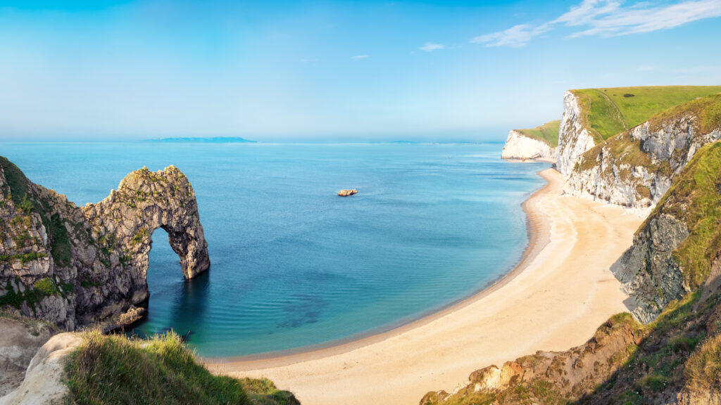 Aerial view of Durdle Door natural rock arch formation with a long sandy beach next to blue sea