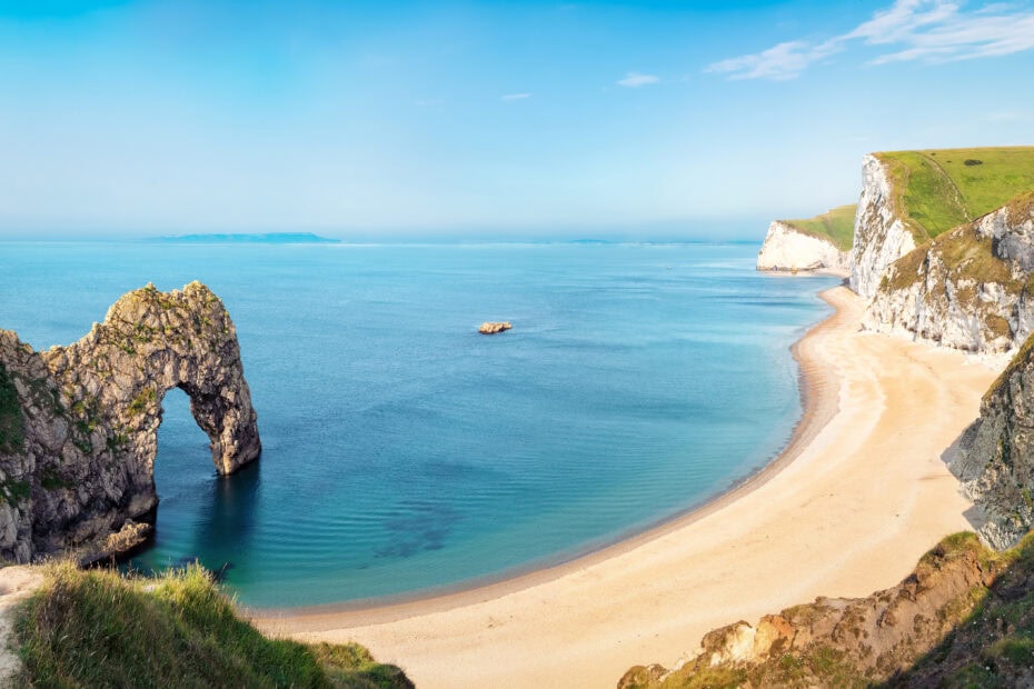 Aerial view of Durdle Door natural rock arch formation with a long sandy beach next to blue sea