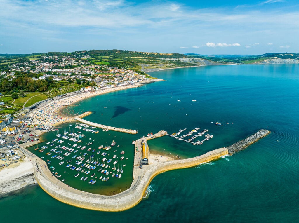 Aerial view of Lyme Regis a small town on the coast in Dorset with a long stone harbour wall extending into the sea. 