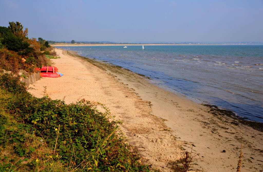 Aerial view of a long sandy beach next to calm flat sea on a sunny day