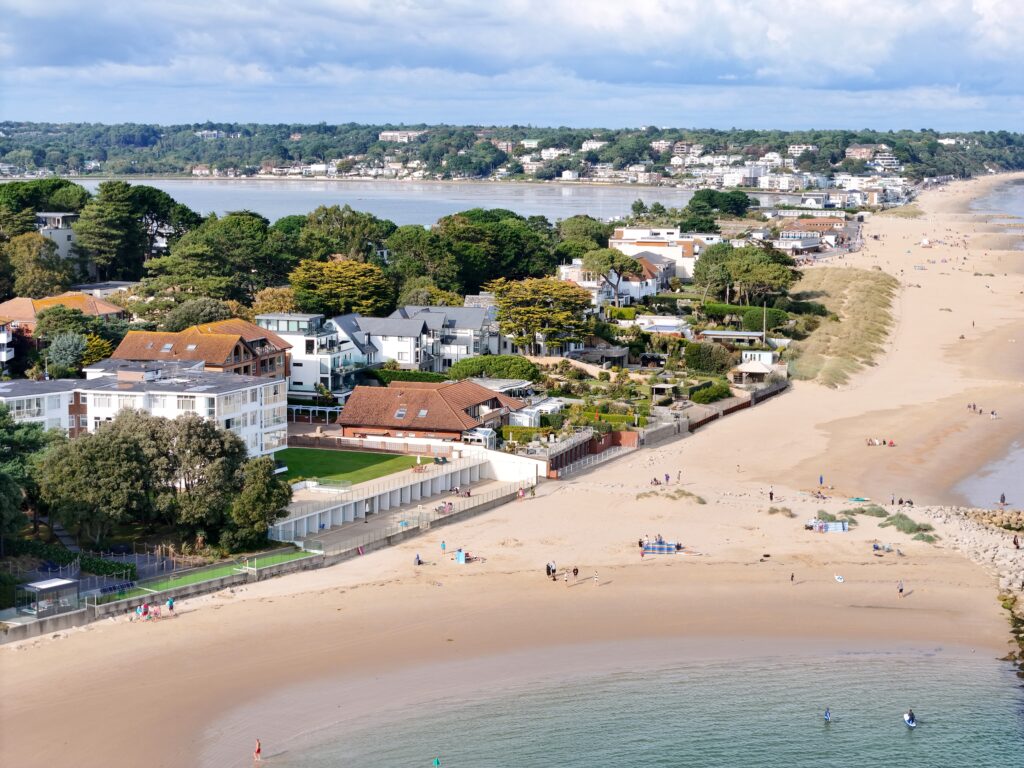Aerial view of a long white sandy beach with expensive houses alongside 