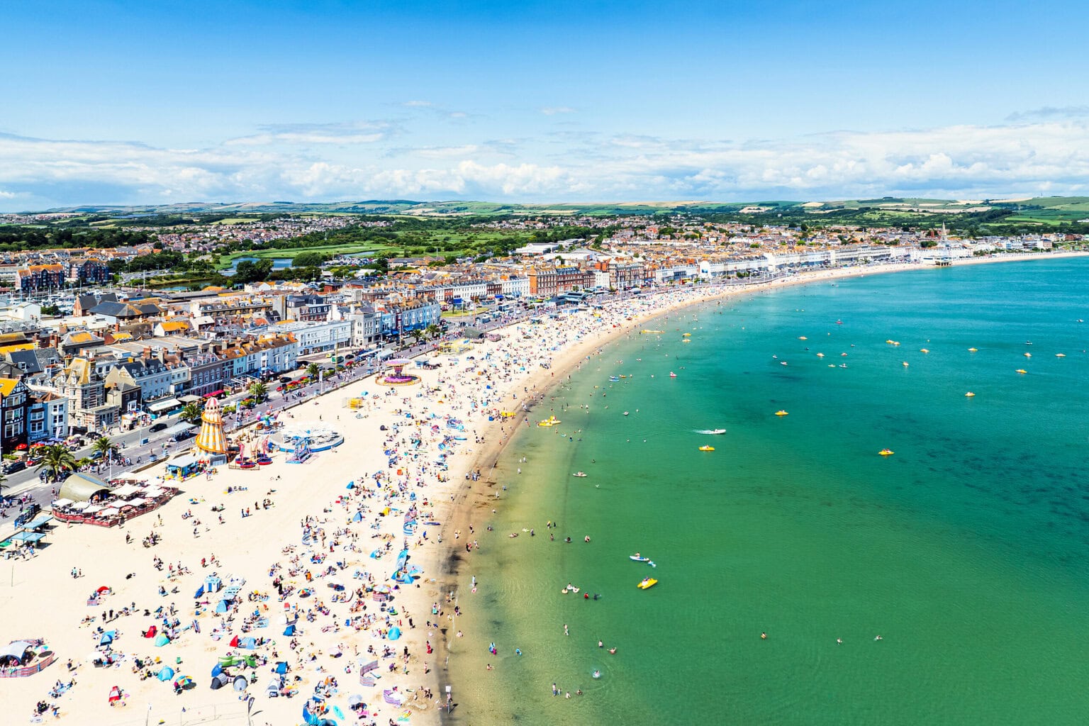 aerial shot of Weymouth beach in summer with pale sand dotted with people next to a large turquoise bay