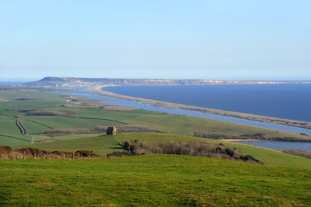 long sandbank with a lagoon on one side and the sea on the other, viewed from the top of a grassy hill - Chesil Beach viewed from Abbotsbury 