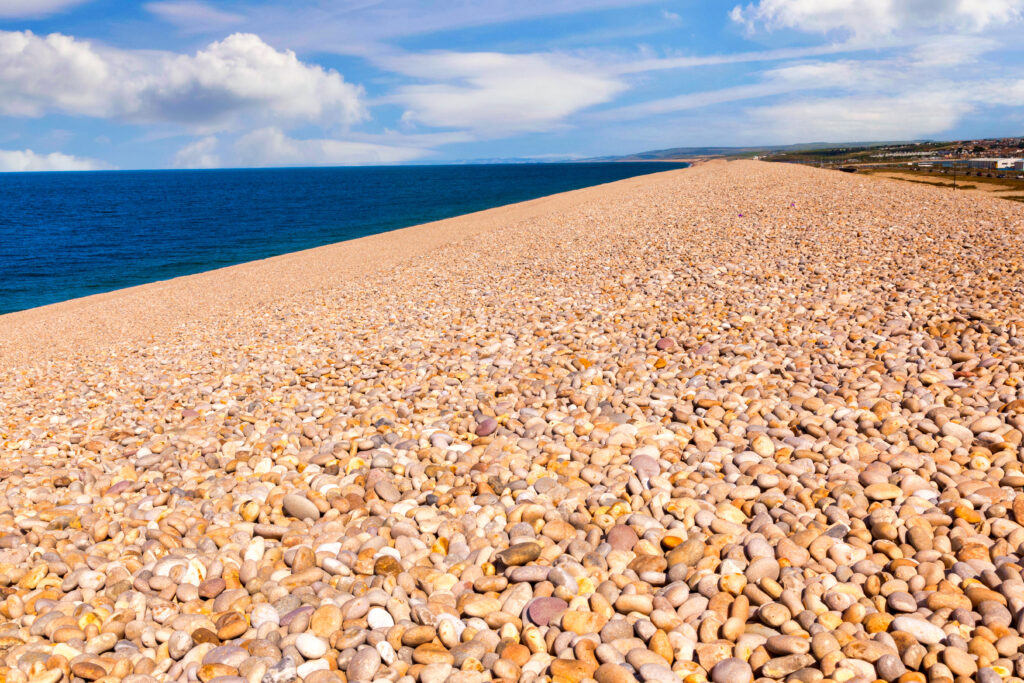 Beach with orange shingle and pebbles next to very blue sea. 