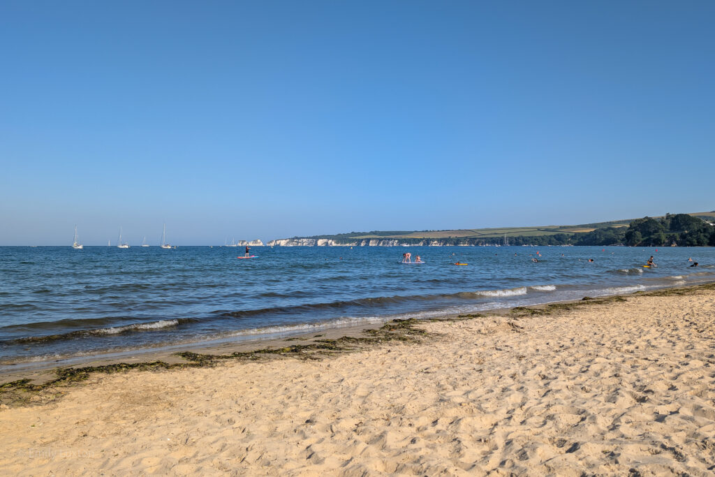 white sandy beach with shallow blue sea and distant cliffs
