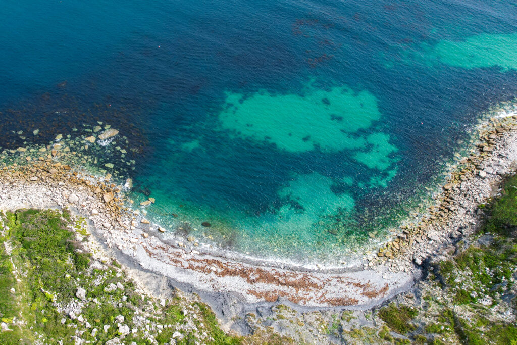 drone shot of 'Little beach' in Portland, grey pebble beach next to turquoise and blue sea. 
