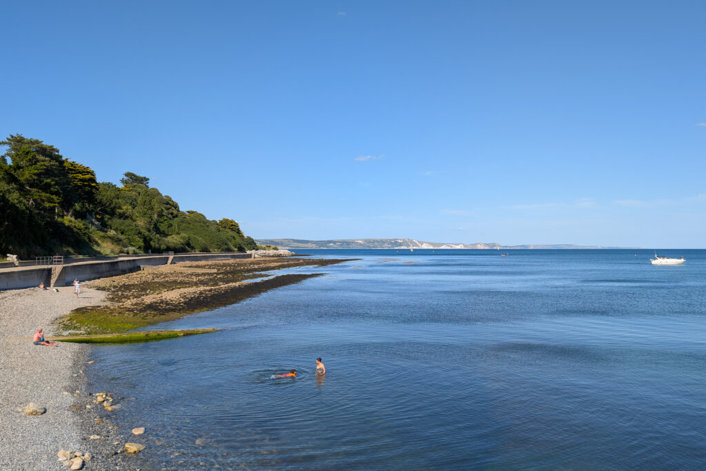 white pebble beach with rocks next to very bright blue sea on a calm sunny day