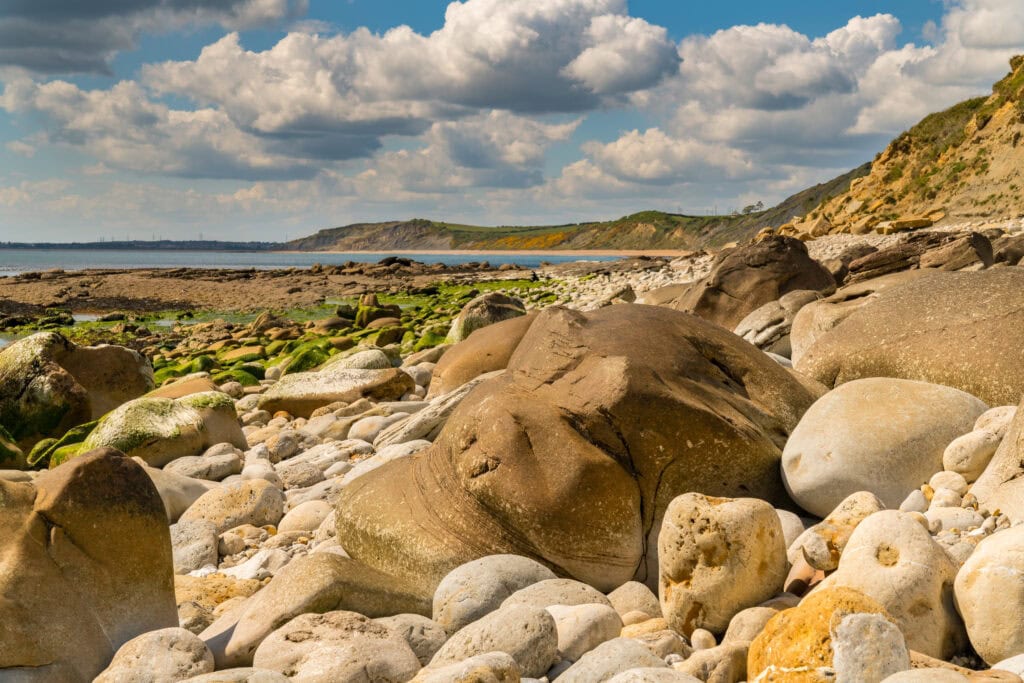 Close up of some orange and brown stones on a beach with the sea behind and rugged cliffs in the distance