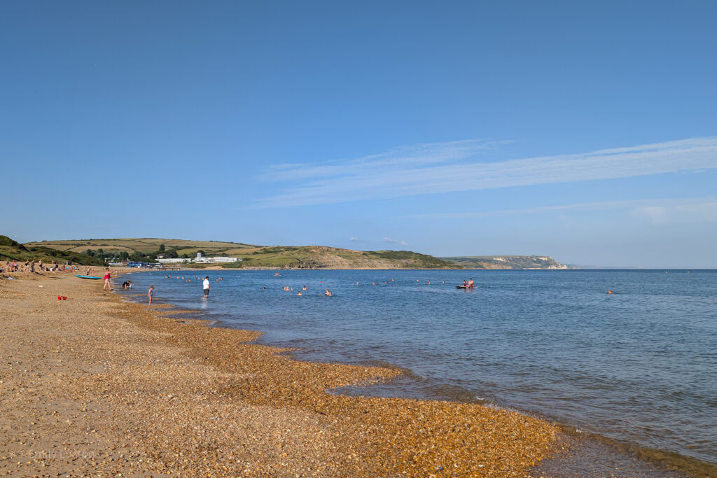 Pebble beach with blue sea and distant grassy cliffs