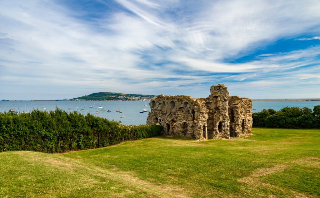 Ruined castle built from grey stone on a cliff edge overlooking the sea with a small island in the distance. 