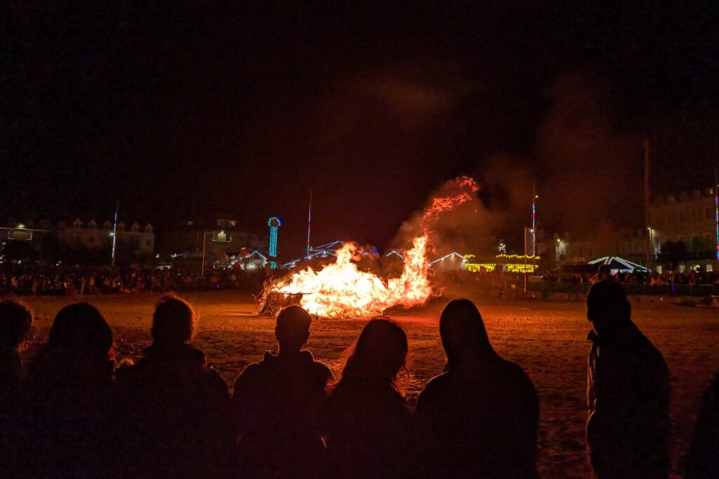 silhouetted people standing in front of a large bonfire on weymouth beach