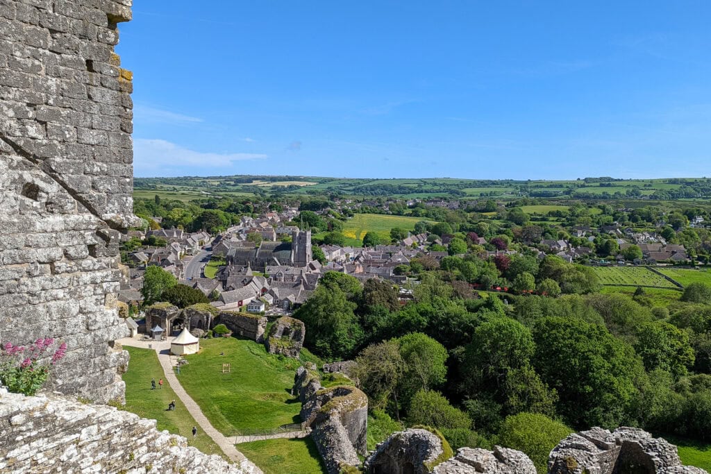 View from a ruined stone castle of lush green countyside and a village | Corfe Castle Dorset in May