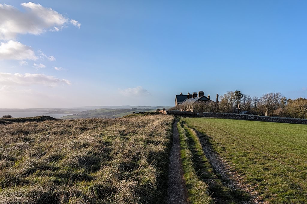 Clifftop path leading along a field towards a row of cottages
