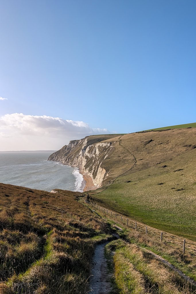 Grassy path leading downhill towards the sea with cliffs in the distance