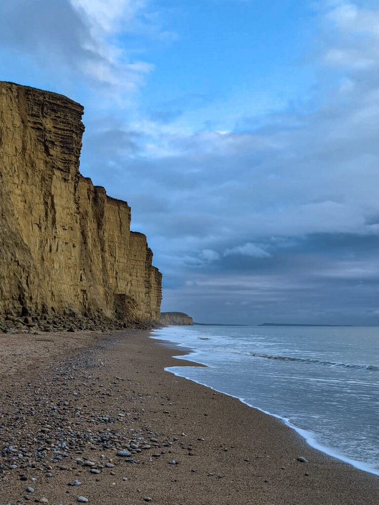 Empty beach with tall yellow sandstone cliffs taken in November at West Bay